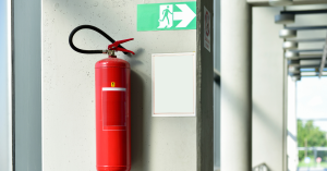 Fire extinguisher hanging on a wall with a fire escape sign above it. 